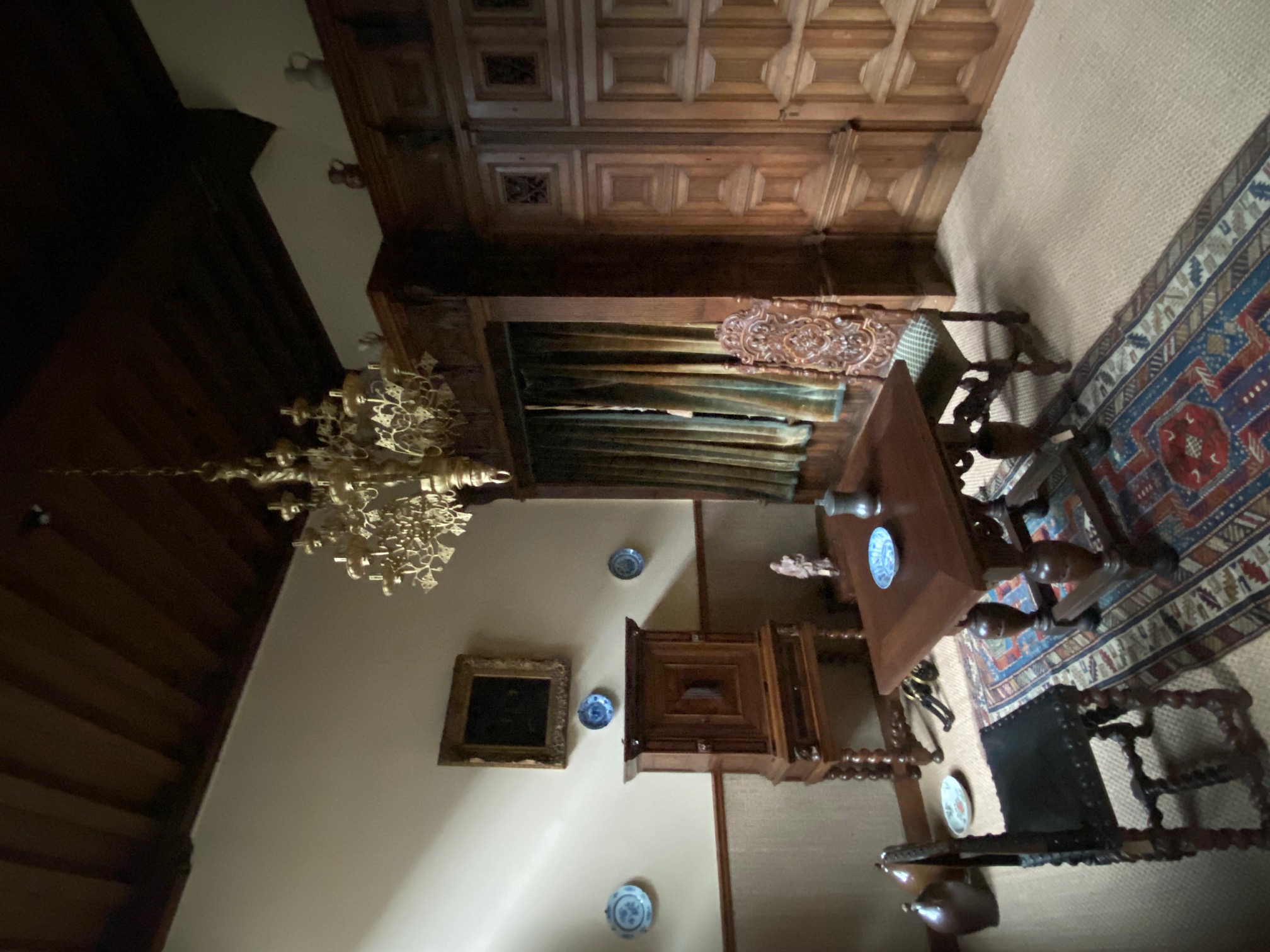 Het interieur van een kamer in het Huis van Meerten. In de kamer staan donkerbruine meubelen, twee stoelen bij een tafel, houten kasten en een klein dressoir. Aan het plafond hangt een kroonluchter.